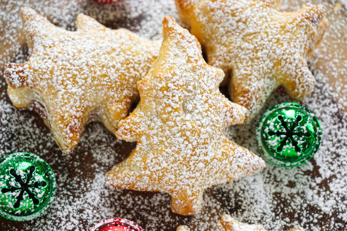 Christmas tree-shaped pastries dusted with powdered sugar are arranged on a surface along with red and green decorative ornaments.