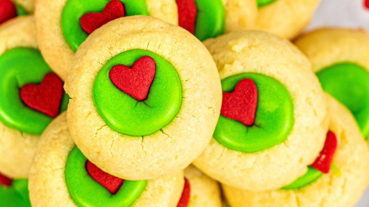 A pile of round sugar cookies with green icing centers, each topped with a small red heart-shaped decoration.