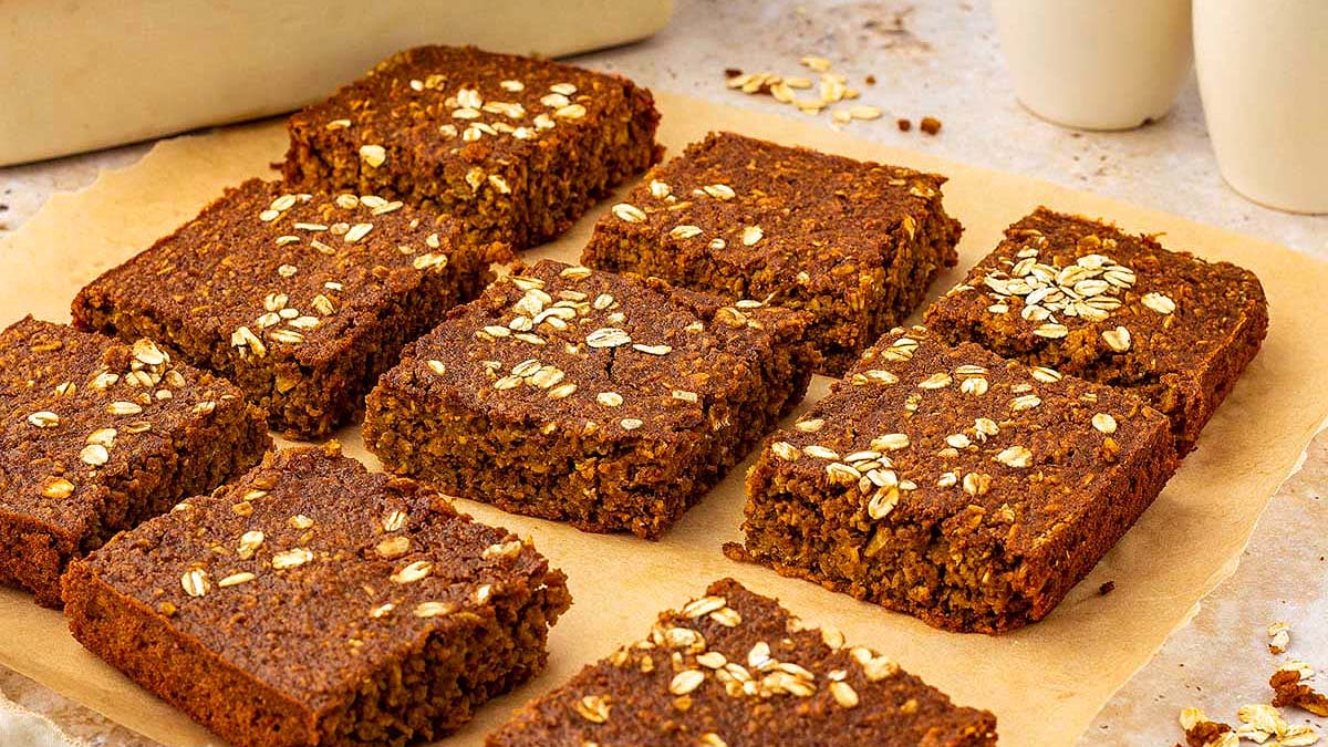 Nine rectangular pieces of oat-topped baked bars are arranged on parchment paper, with one bar slightly separated from the group.