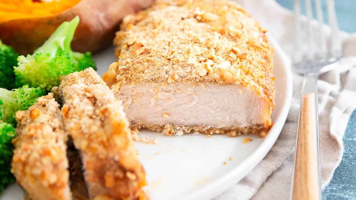 A breaded pork chop sliced on a white plate, served with broccoli and a baked sweet potato.