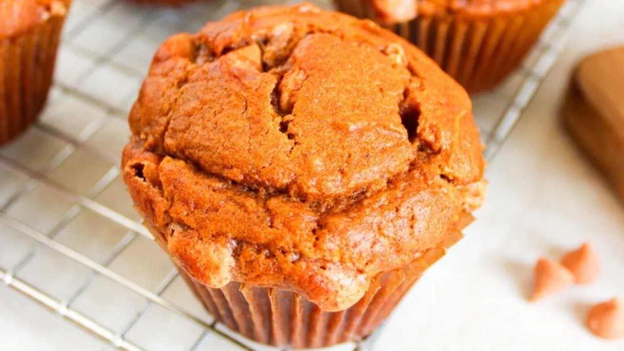 A close-up of a baked muffin with a golden-brown top, resting on a metal cooling rack.