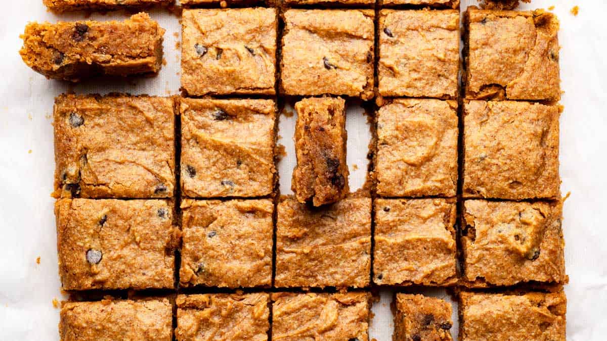 A batch of chocolate chip blondies cut into squares, with one square partially removed and another turned on its side.