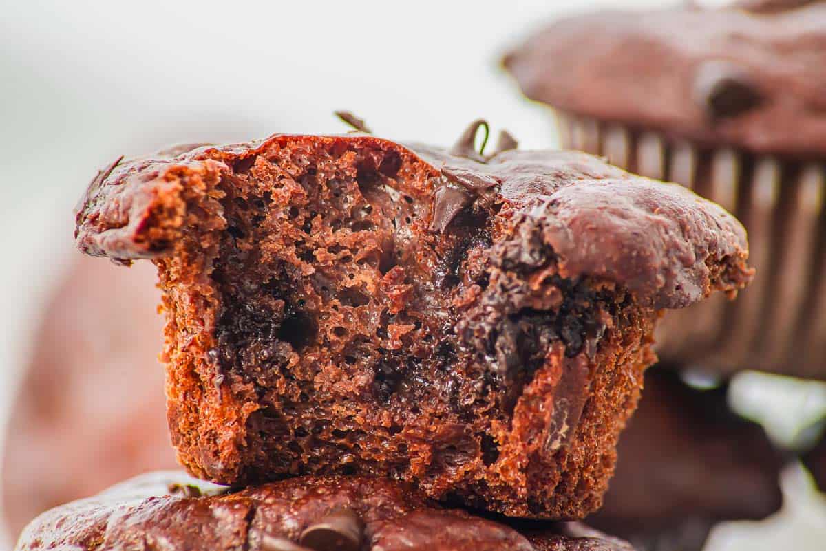 A close-up of a chocolate muffin with a bite taken out, showing a moist, chocolatey interior with visible chocolate chips.