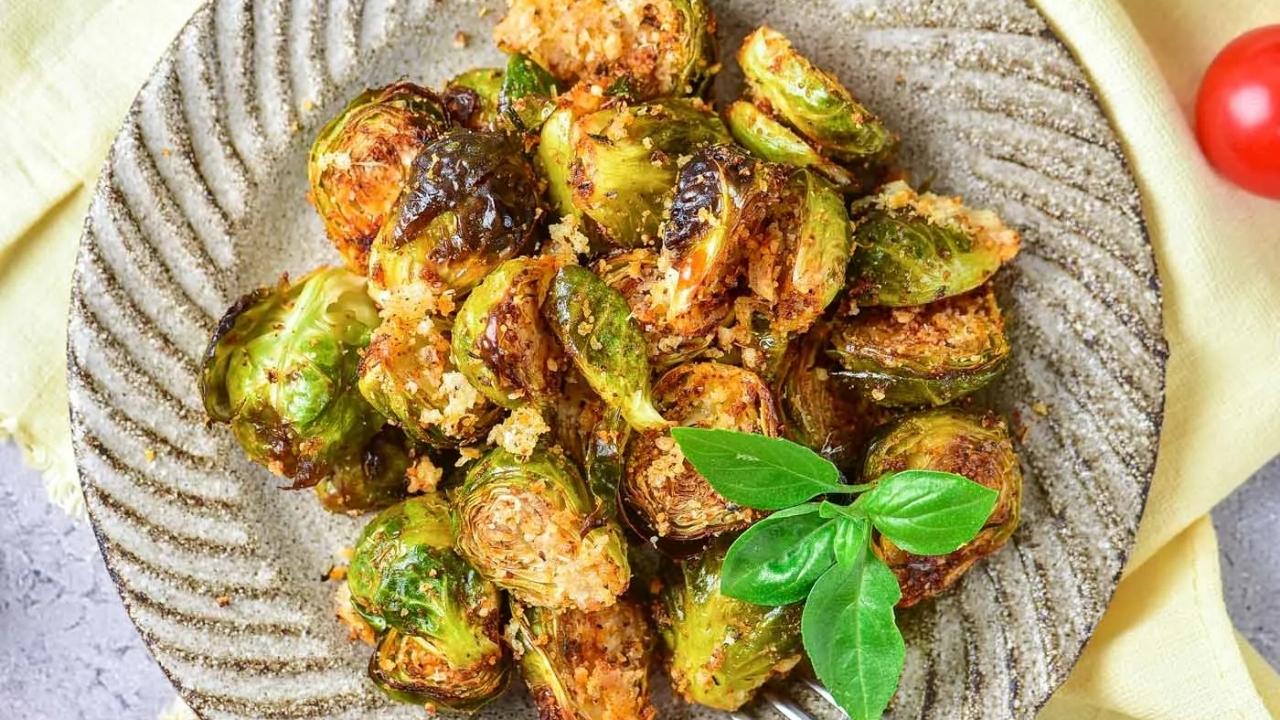 A plate of roasted Brussels sprouts garnished with fresh basil, served on a textured ceramic dish with a yellow cloth underneath.