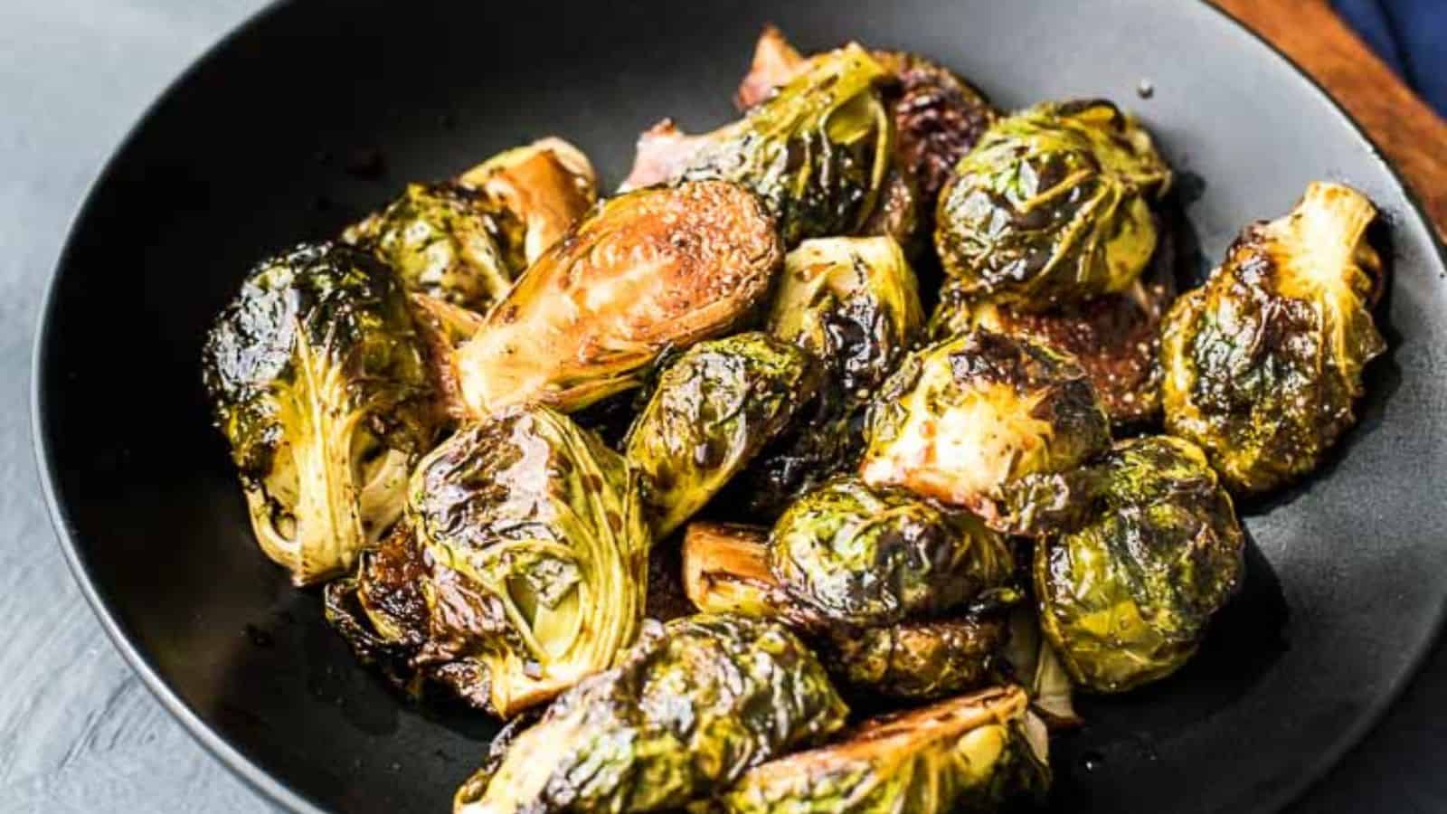 A black bowl filled with roasted Brussels sprouts, some halved and some whole, lightly browned and seasoned.