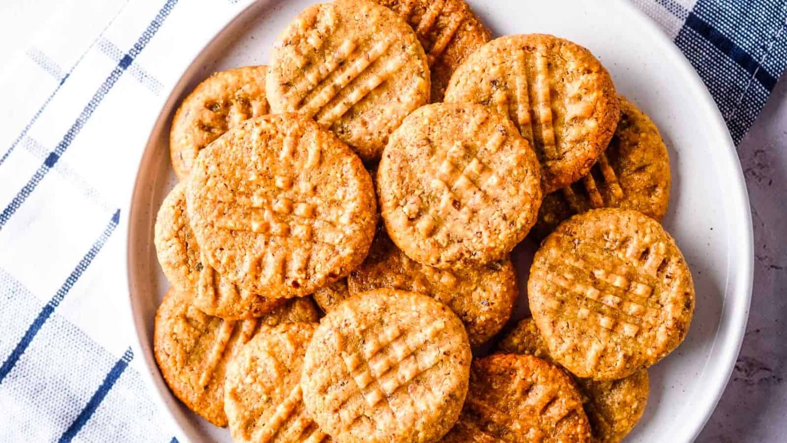 A white plate filled with round, golden brown cookies marked with a crisscross fork pattern, set on a blue and white checkered cloth.