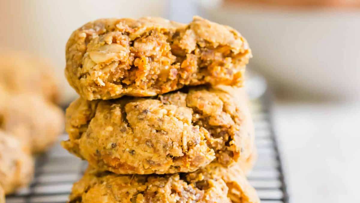 Three chunky oatmeal cookies are stacked on a cooling rack, with a bite taken out of the top cookie.