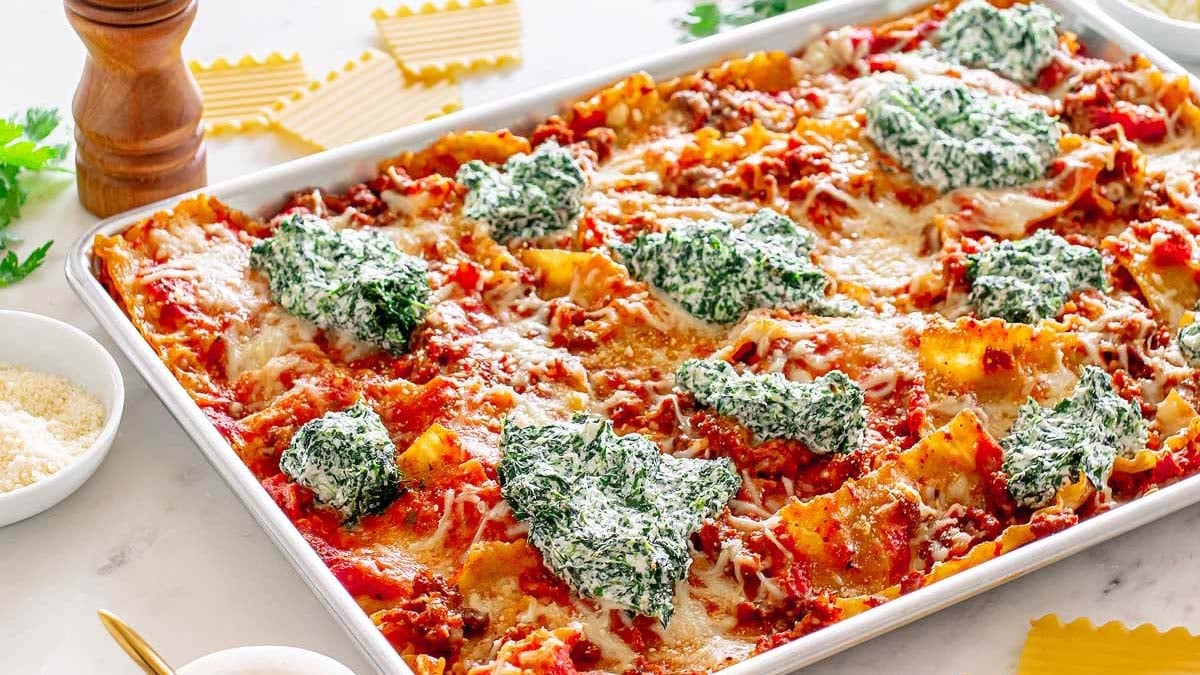 A baked lasagna in a rectangular pan topped with tomato sauce, melted cheese, and dollops of spinach and ricotta mixture.