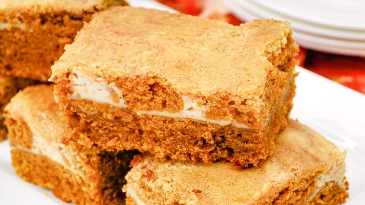 Close-up of three stacked pumpkin bars with a creamy filling and a golden-brown top, served on a white plate.