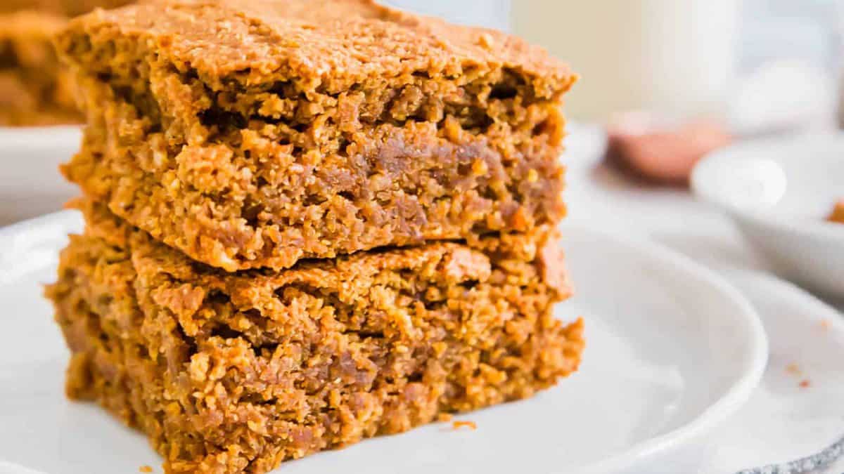 Two pieces of baked oat bars stacked on a white plate, showing a dense and textured interior.