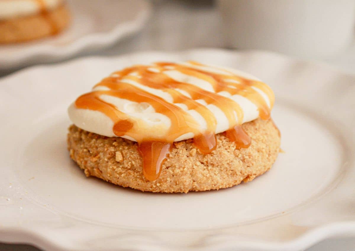 A round cookie topped with a layer of whipped cream and drizzled with caramel sauce on a white plate.