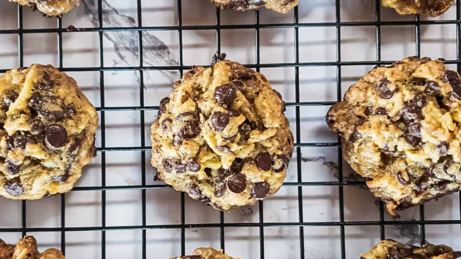 Chocolate chip cookies cooling on a black wire rack, viewed from above, with a marble surface underneath.