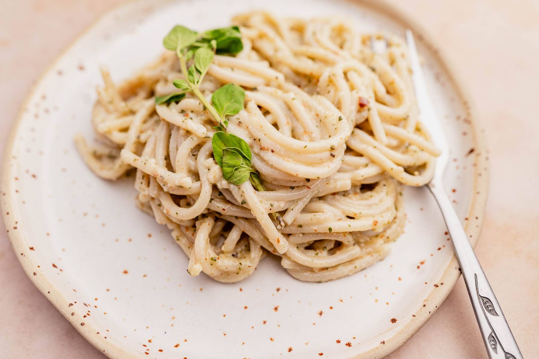 A plate of spaghetti coated in a creamy sauce, garnished with fresh green herbs, with a fork resting on the side.