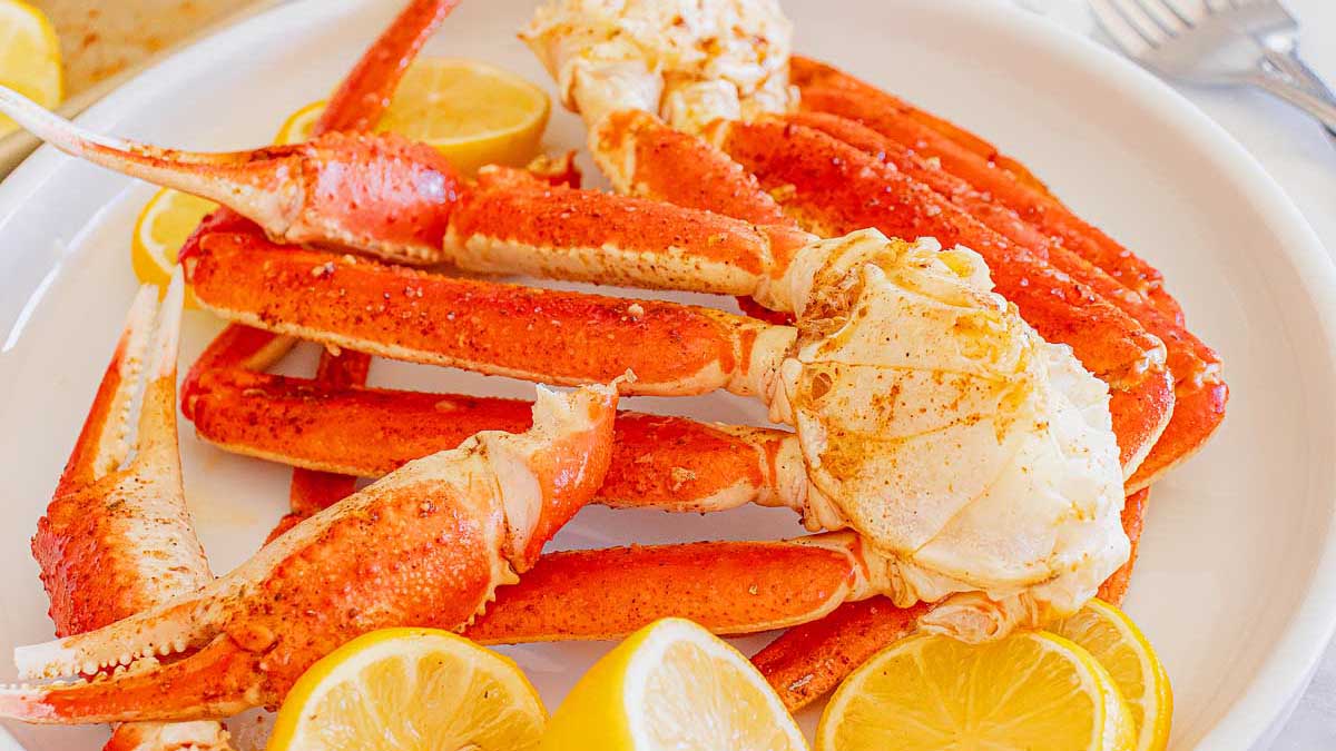 A plate of cooked crab legs seasoned with spices, served with lemon wedges on a white dish.