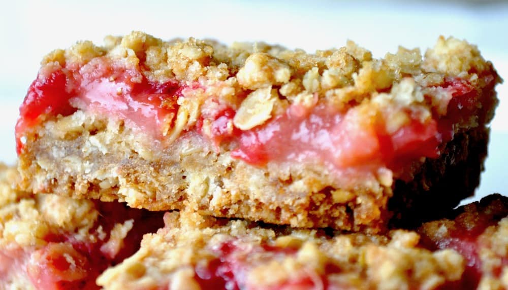 Close-up of two fruit crumble bars with a golden oat crumb topping and a pinkish-red fruit filling.