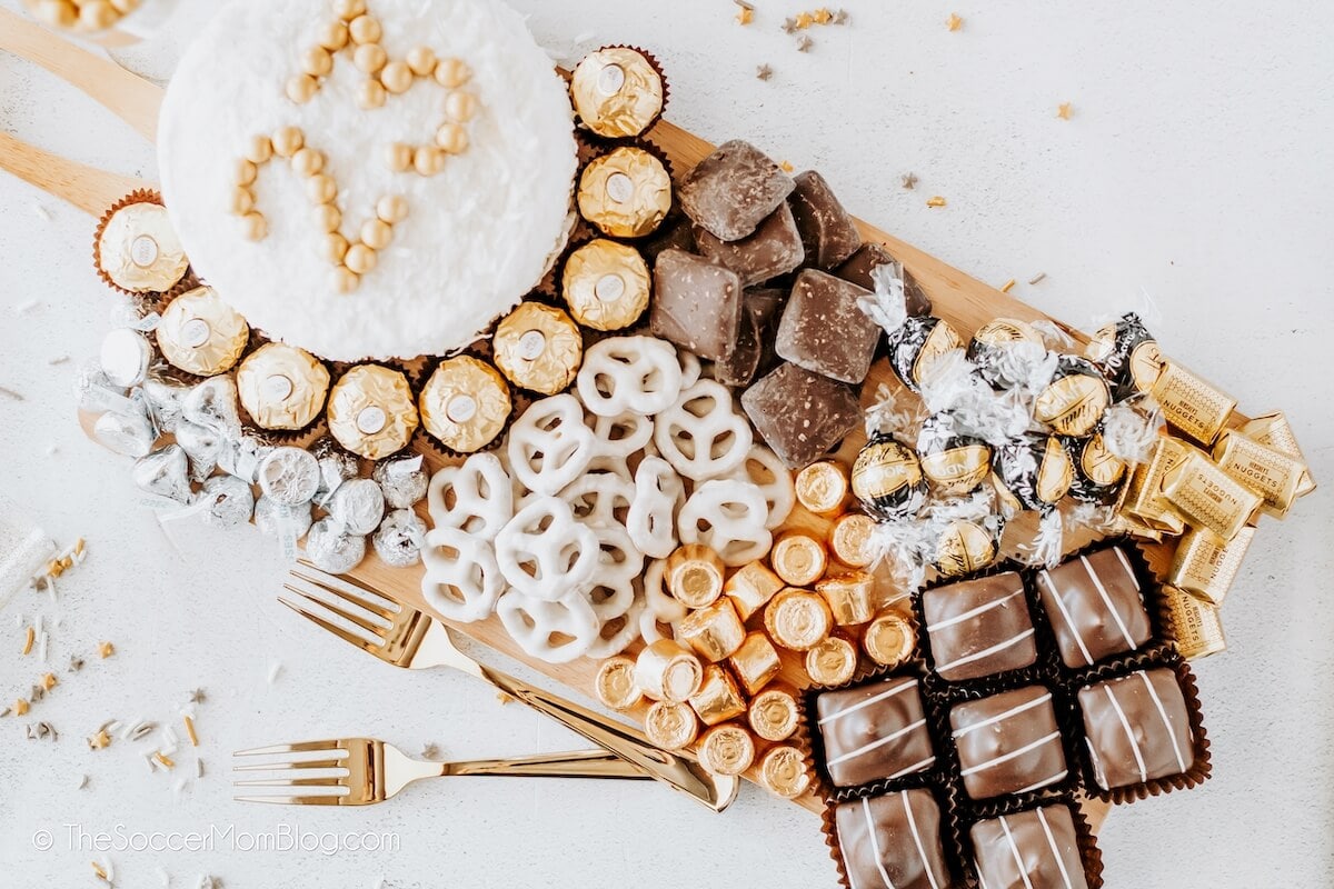 A white plate holds cookies decorated as a clock face with numbers 1 to 12. Two cookies form clock hands pointing at midnight. Silver and white ribbons surround the plate.