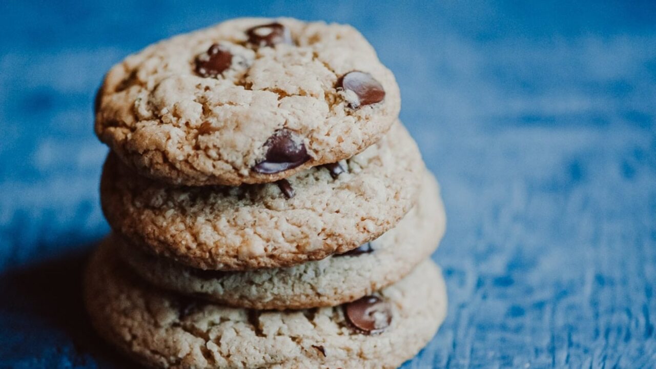 A stack of four chocolate chip cookies is arranged on a blue wooden surface.