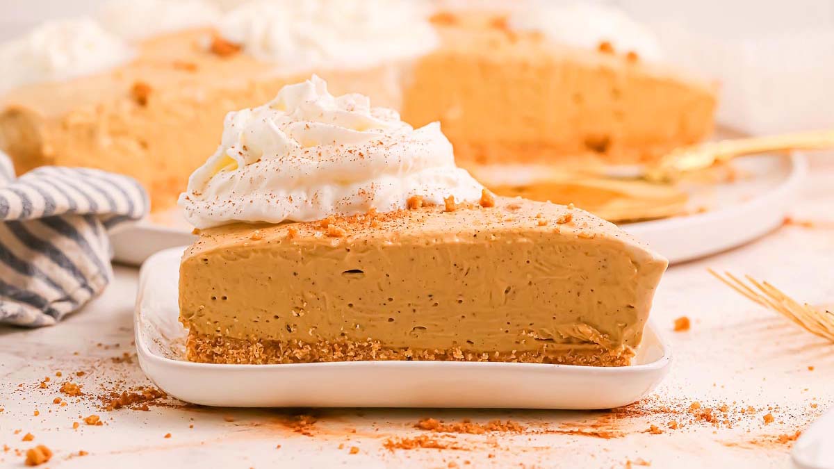 A slice of creamy peanut butter pie with a graham cracker crust and whipped cream on top, served on a white plate.