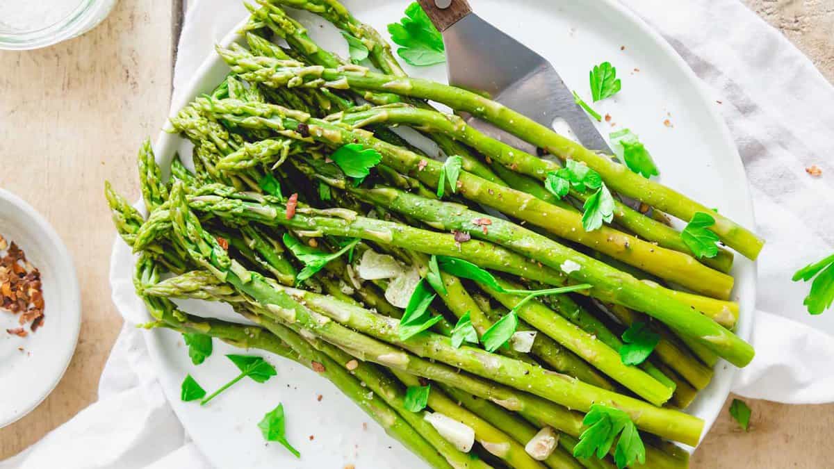 Steamed asparagus spears garnished with fresh parsley and garlic slices on a white plate.