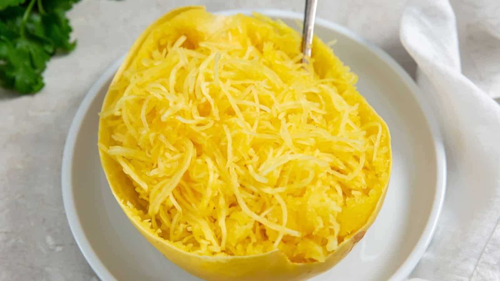 Half of a cooked spaghetti squash with its flesh scraped into noodle-like strands, served on a white plate with a fork inserted.