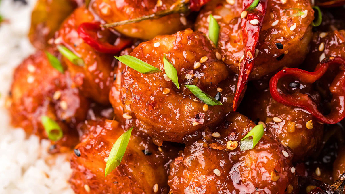 Close-up of spicy glazed shrimp garnished with sliced green onions and sesame seeds, served with white rice.