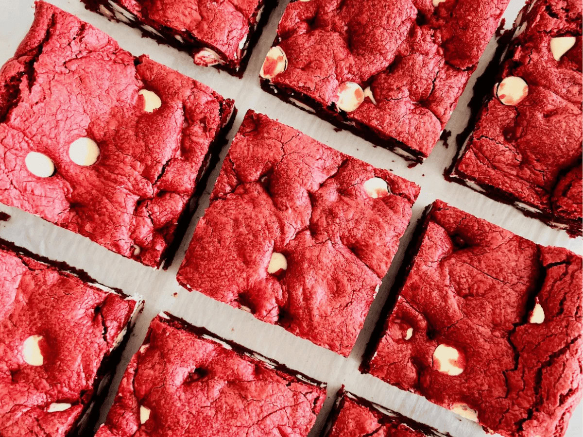 Nine square pieces of red velvet brownies with visible white chocolate chips, arranged neatly on a white surface.