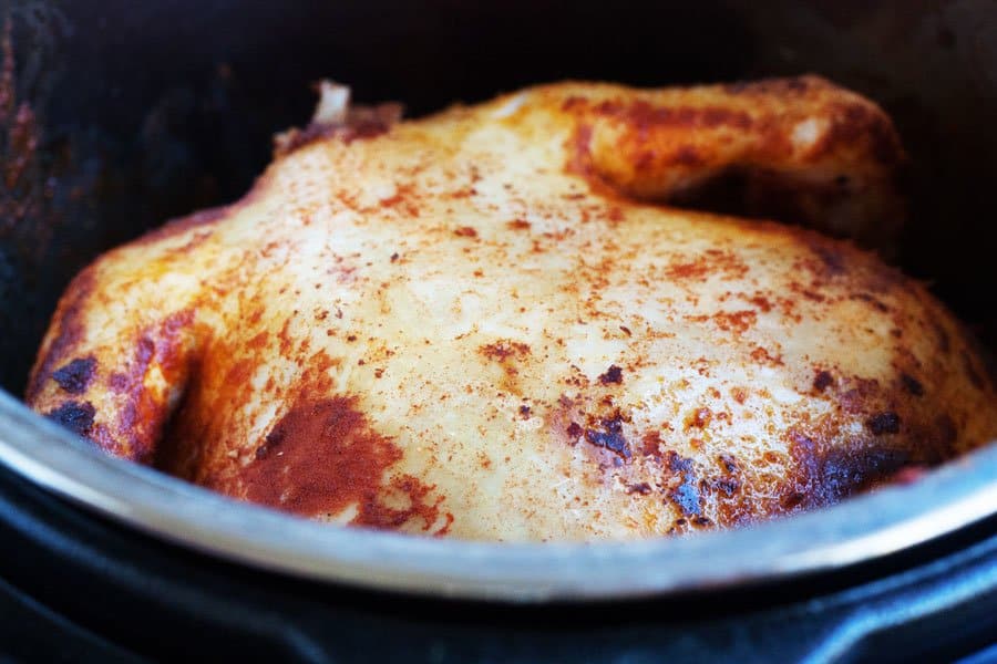 A whole seasoned chicken is cooking inside a metal pot, with visible spices on the skin.