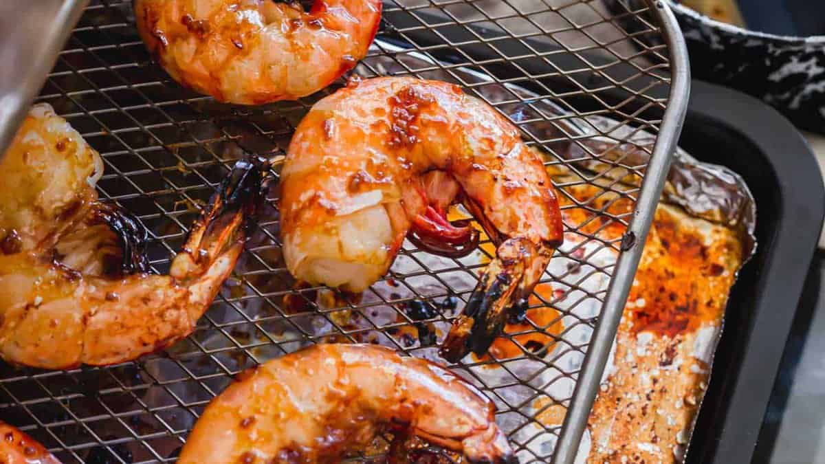 Grilled shrimp with a glaze on a wire rack over a baking tray, showing cooked, slightly charred surfaces.