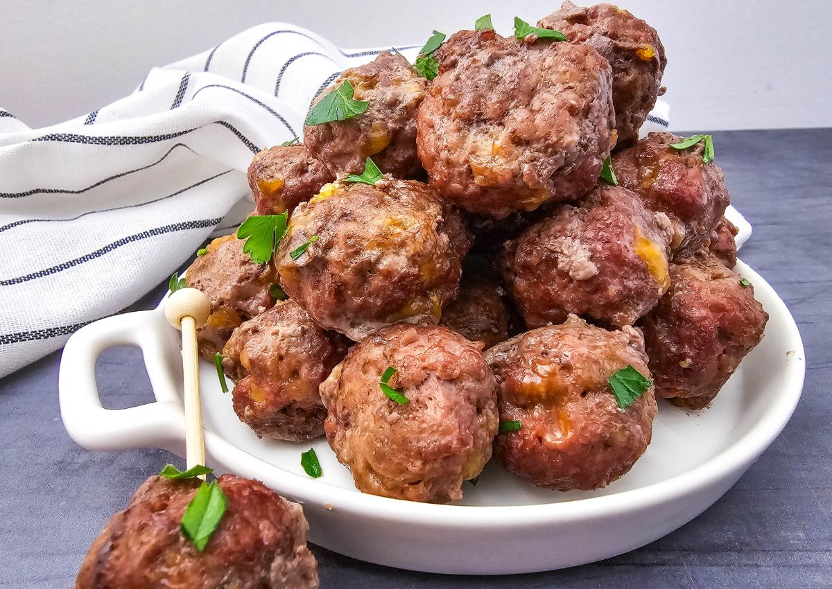A white plate holds a pile of cooked meatballs garnished with chopped herbs, with a striped cloth in the background.