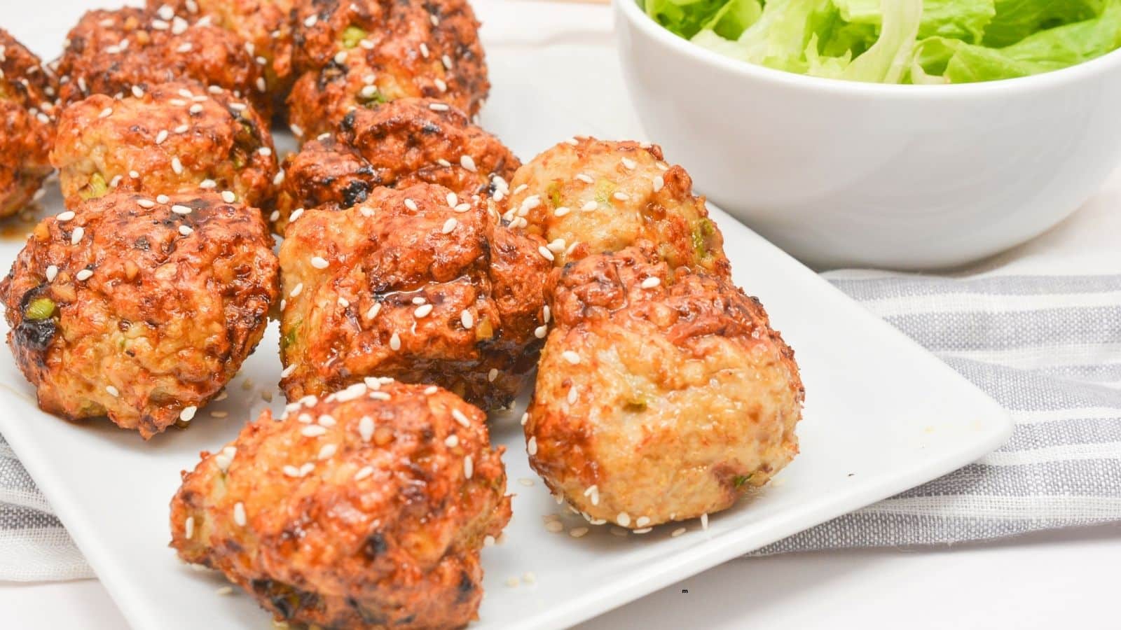 A white plate with several browned, sesame-topped vegetable fritters next to a bowl of leafy green salad.