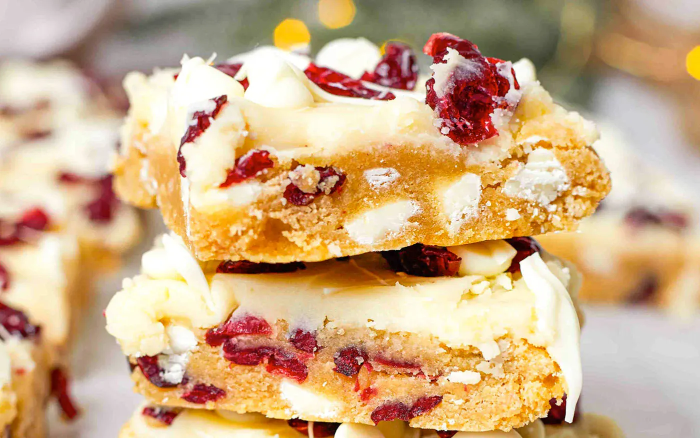 Three stacked dessert bars with white chocolate chips and dried cranberries, topped with white frosting and more cranberries.