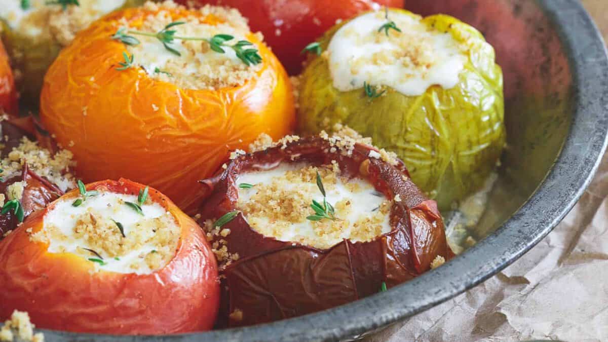 Assorted stuffed tomatoes and peppers filled with a creamy mixture and topped with breadcrumbs and fresh herbs, baked in a round metal dish.