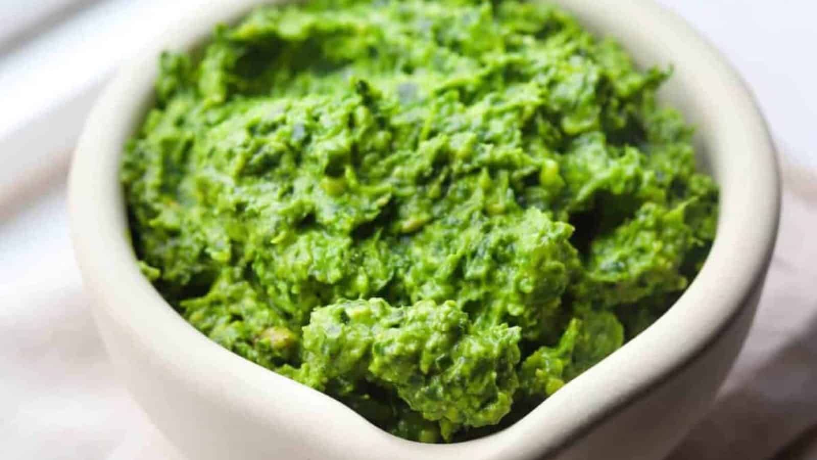 A white bowl filled with bright green, mashed guacamole placed on a light-colored surface.