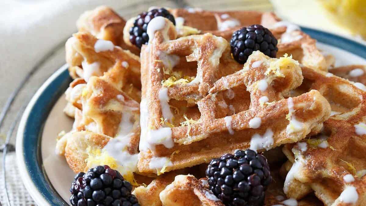 A plate of waffles topped with icing, lemon zest, and fresh blackberries.