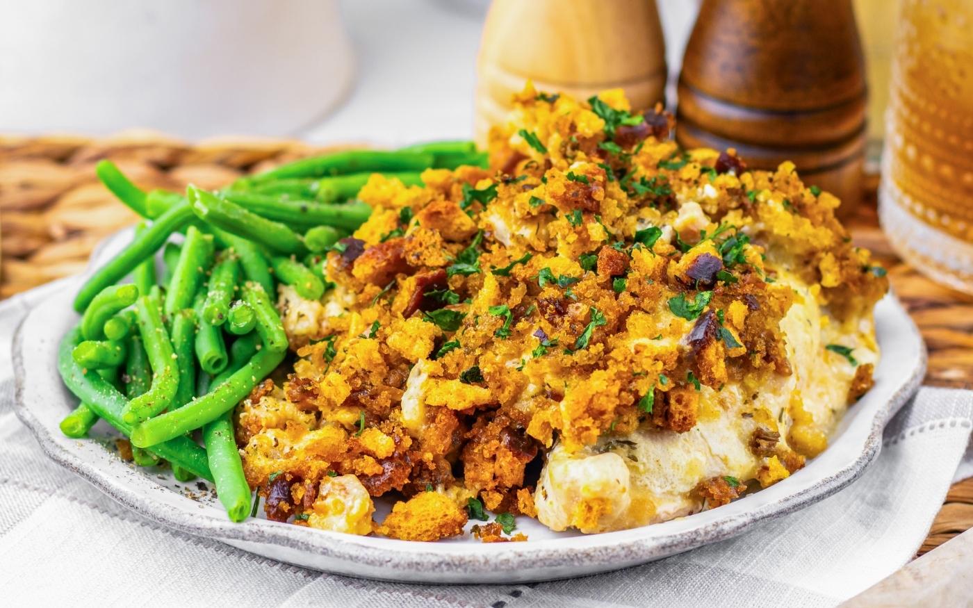 A plate with green beans and a serving of casserole topped with browned breadcrumbs, garnished with chopped parsley. Salt and pepper shakers are in the background.