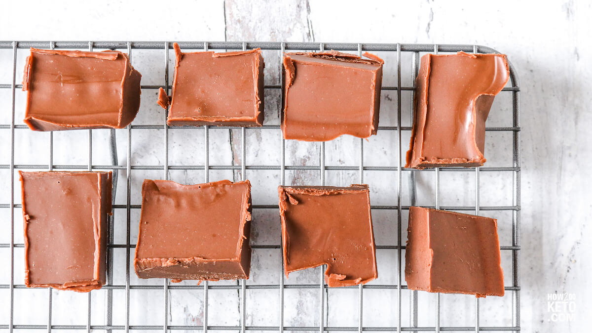 Eight square pieces of chocolate fudge are arranged on a metal cooling rack with a white surface underneath.