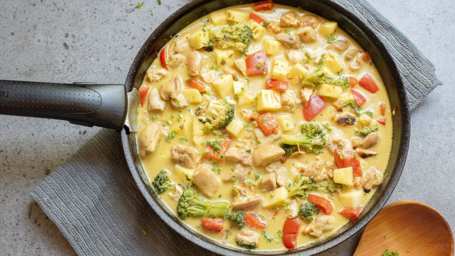 A skillet filled with a creamy chicken and vegetable curry containing chunks of chicken, broccoli, red bell pepper, and potatoes.
