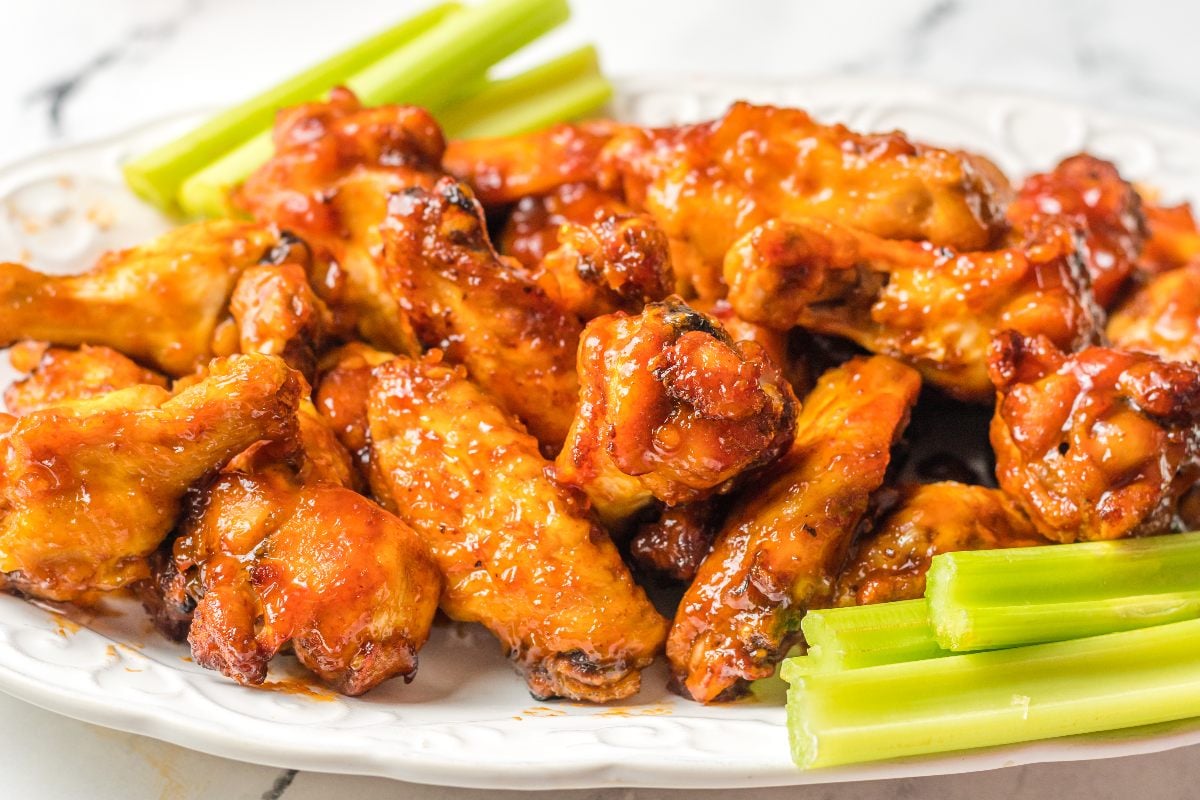 A plate of glazed chicken wings served with celery sticks on a white dish.