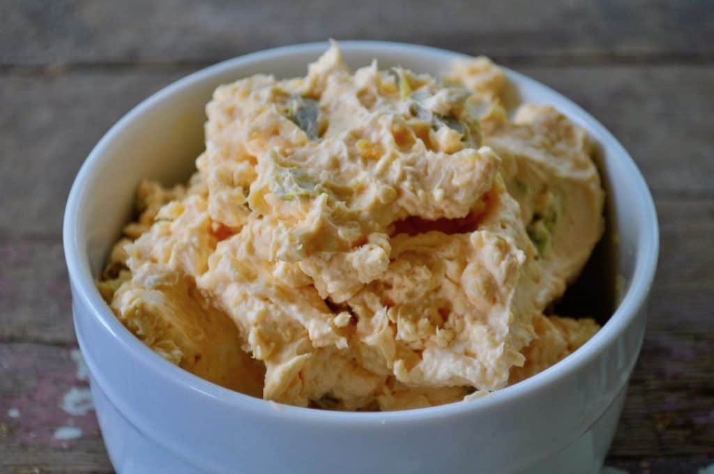 A white bowl filled with a creamy orange cheese spread with visible chunks of pickles.