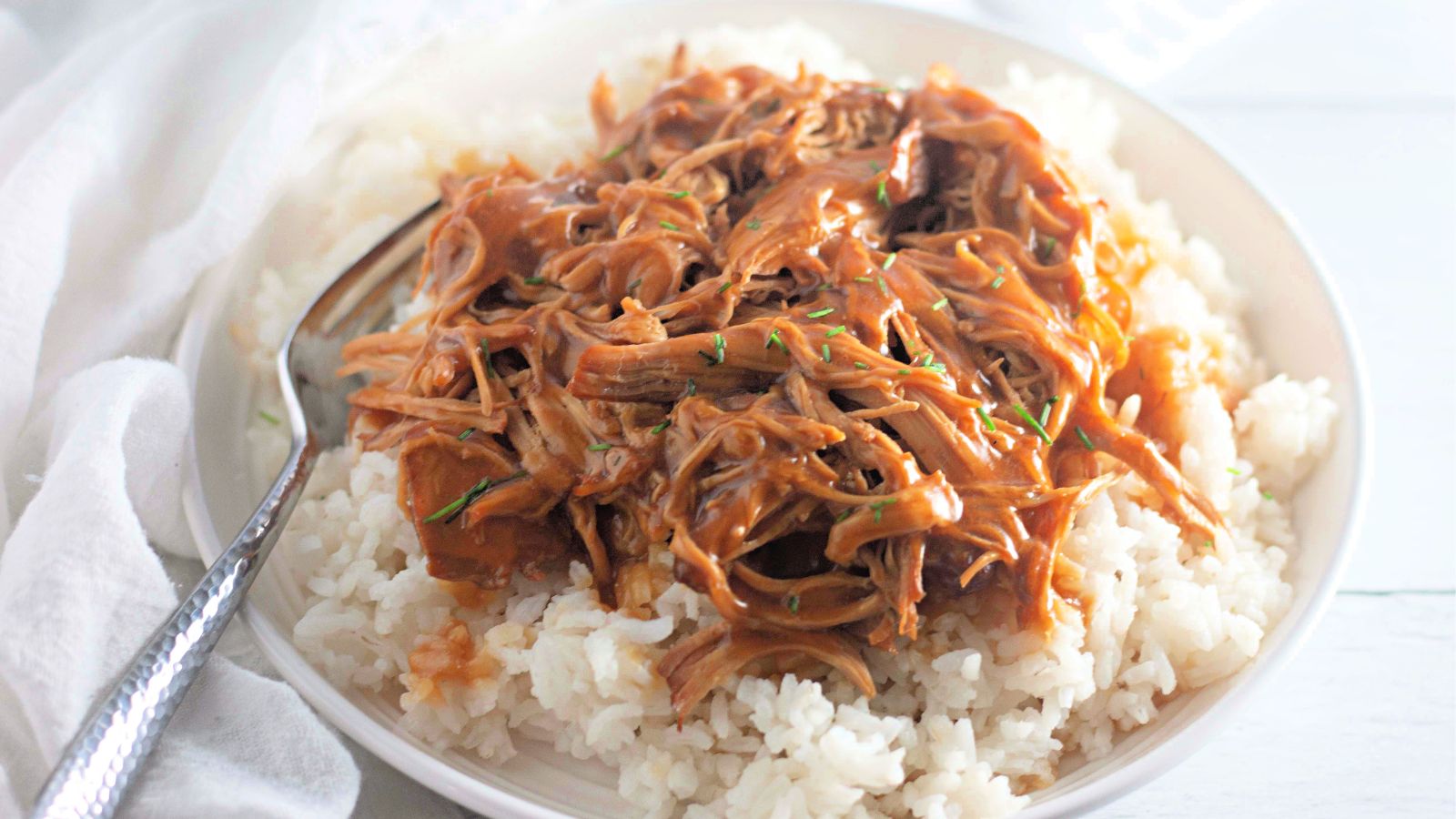 A plate of white rice topped with shredded meat in a brown sauce, with a spoon resting on the side.