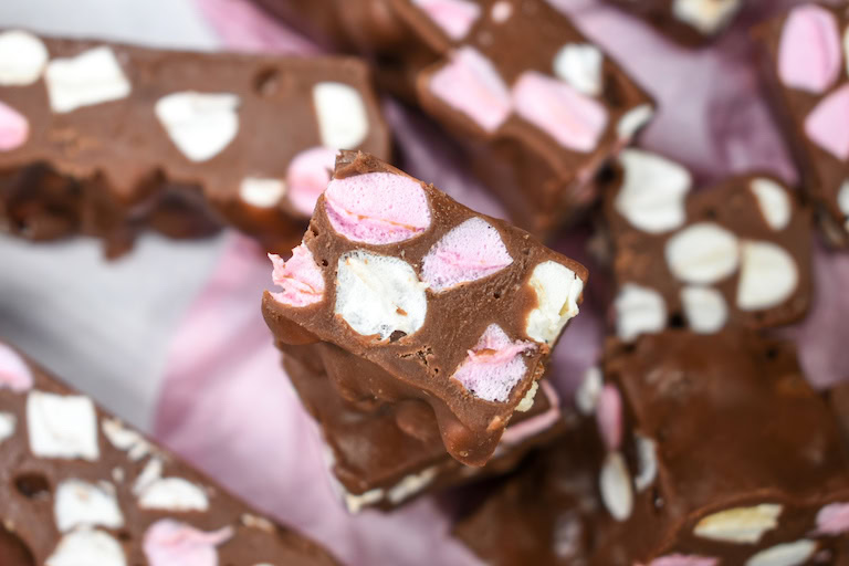 Close-up of chocolate fudge pieces with pink and white mini marshmallows mixed inside, stacked on a surface.