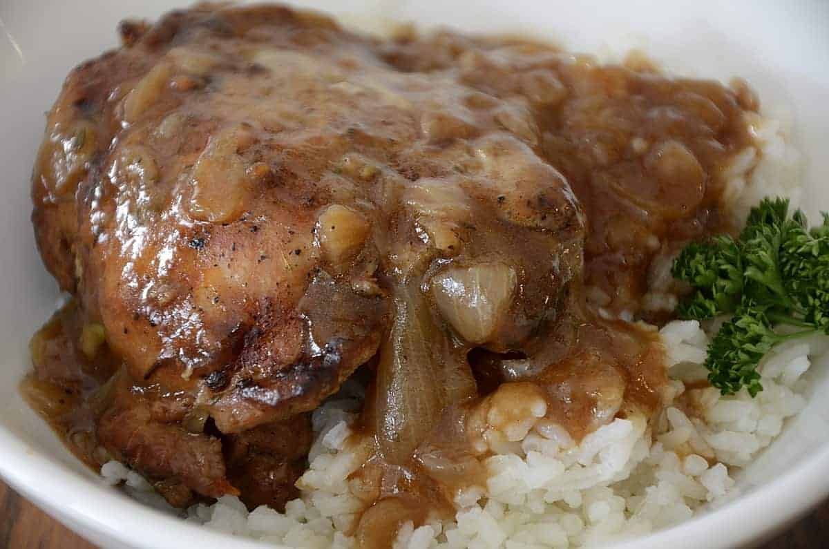 A piece of chicken covered in brown onion gravy served over white rice, with a small sprig of parsley on the side.