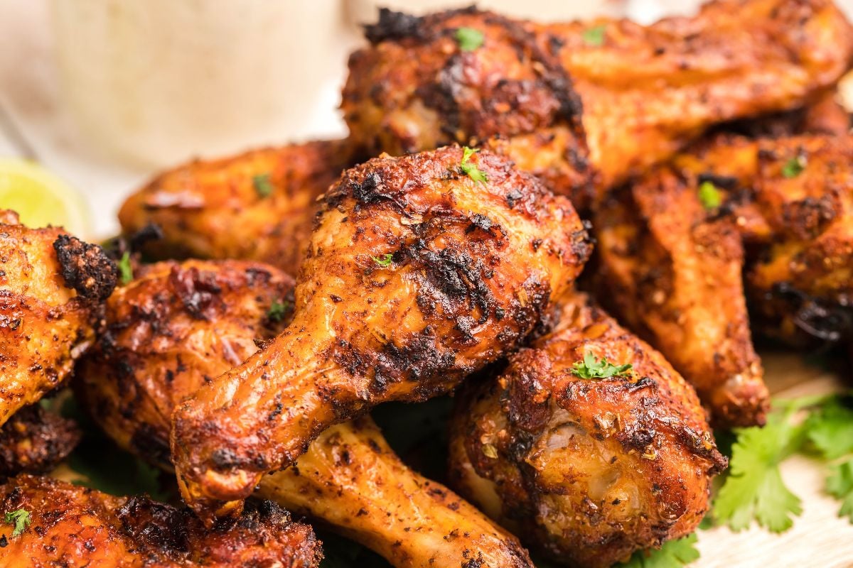 A close-up of several grilled chicken drumsticks garnished with herbs, showing a crispy, charred exterior.
