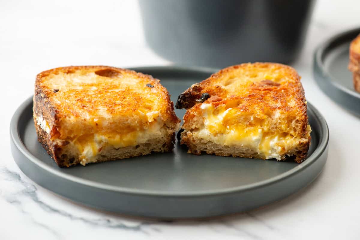 A grilled cheese sandwich cut in half sits on a gray plate, showing melted cheese between slices of toasted bread.