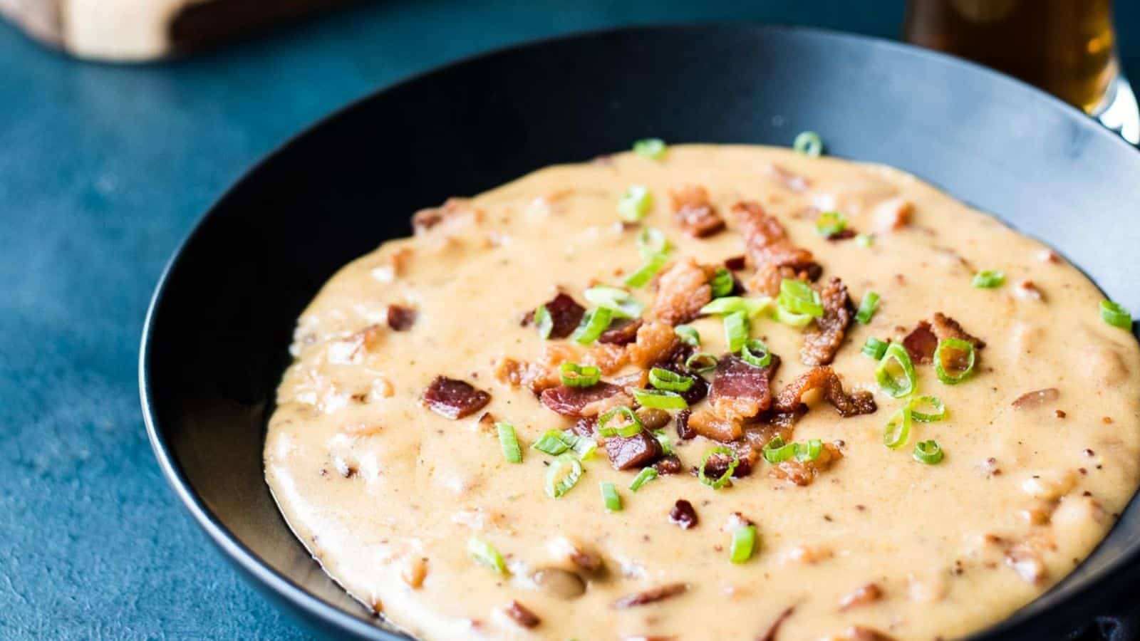 A black bowl filled with creamy soup topped with chopped bacon and green onions, placed on a dark surface.