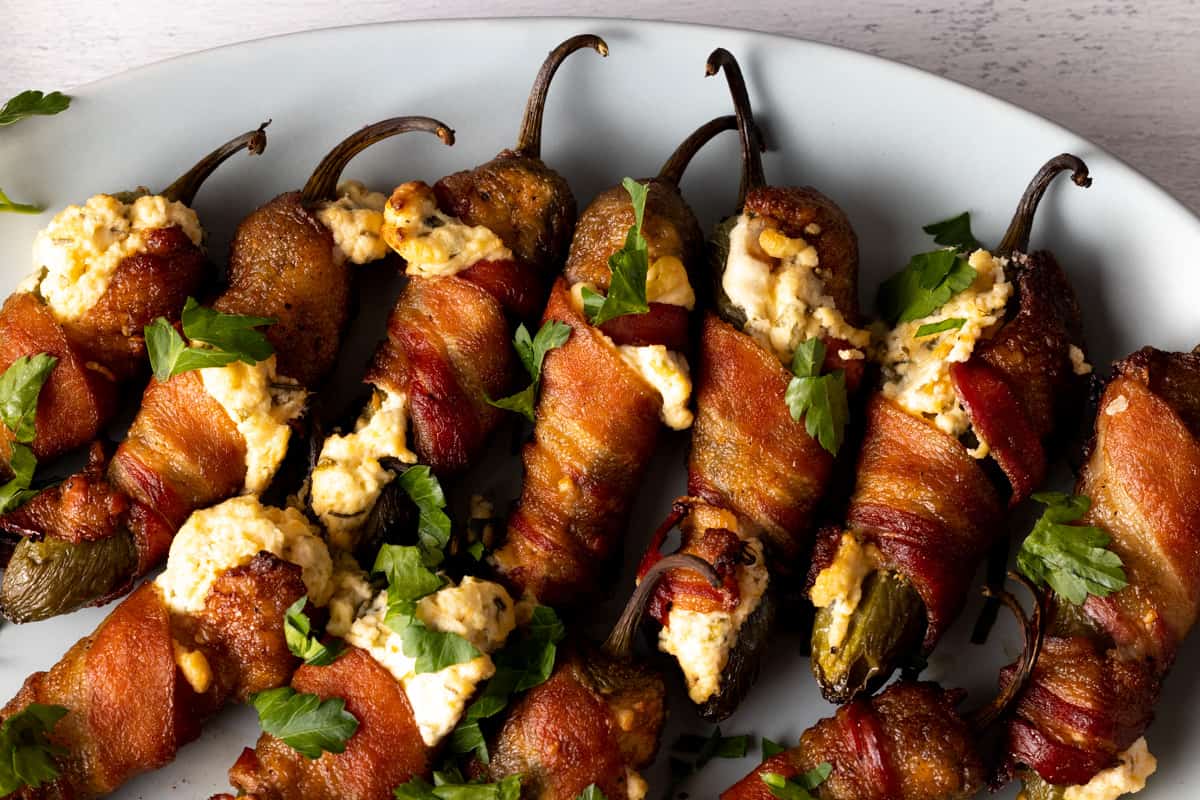 A plate of bacon-wrapped, cheese-stuffed jalapeรฑo poppers garnished with chopped parsley.