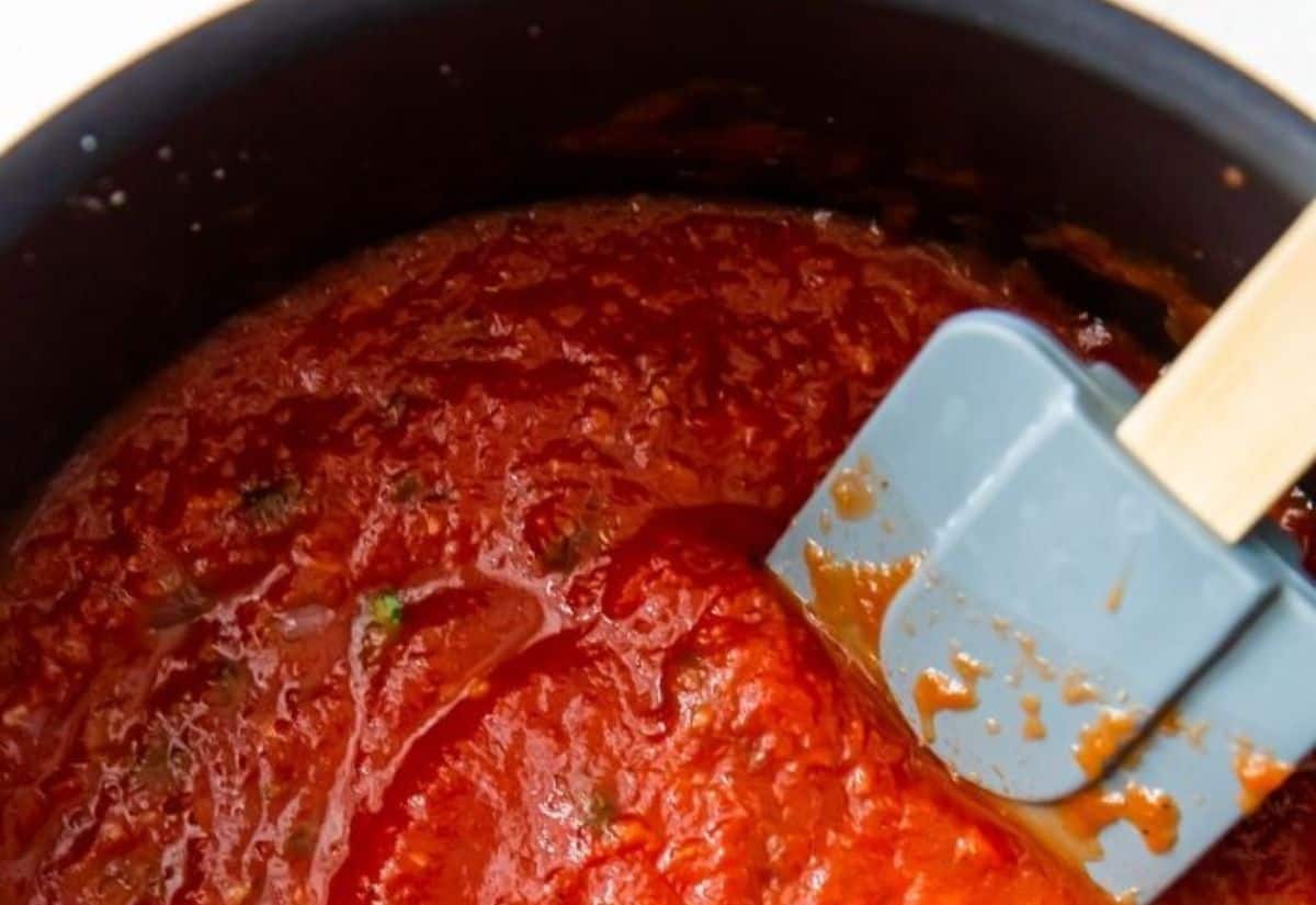 A pot of red tomato sauce being stirred with a grey silicone spatula.