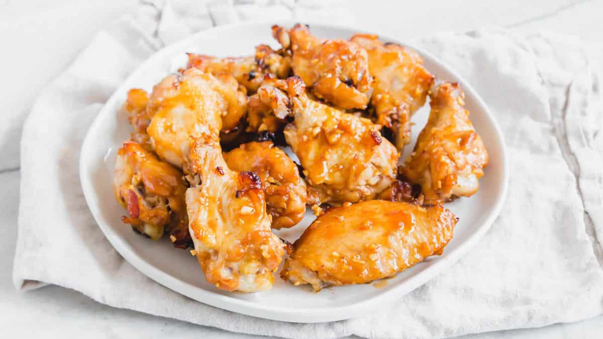 A white plate filled with glazed chicken wings sits on a light-colored cloth on a marble surface.