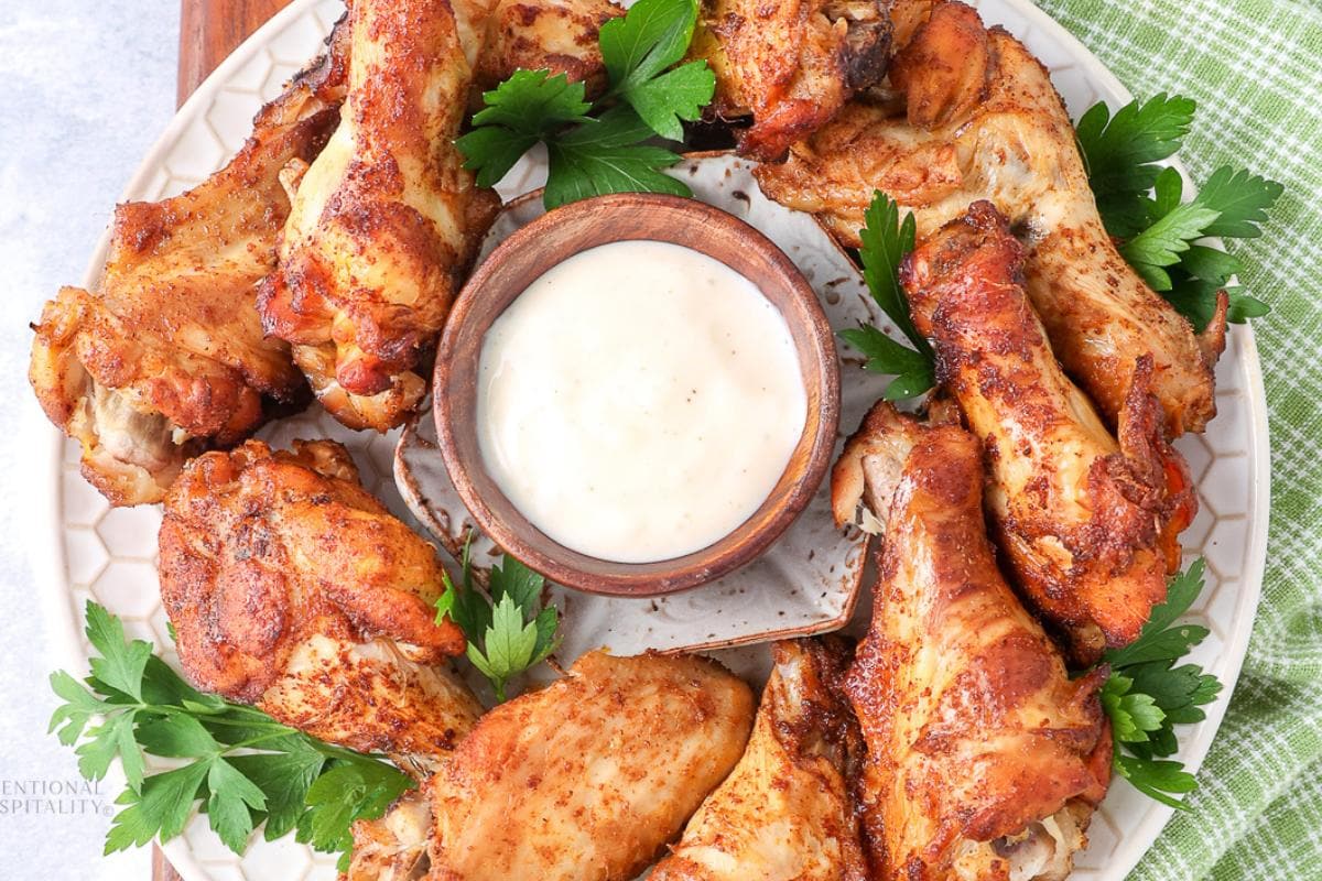 A plate of cooked chicken wings arranged around a bowl of creamy dipping sauce, garnished with fresh parsley.