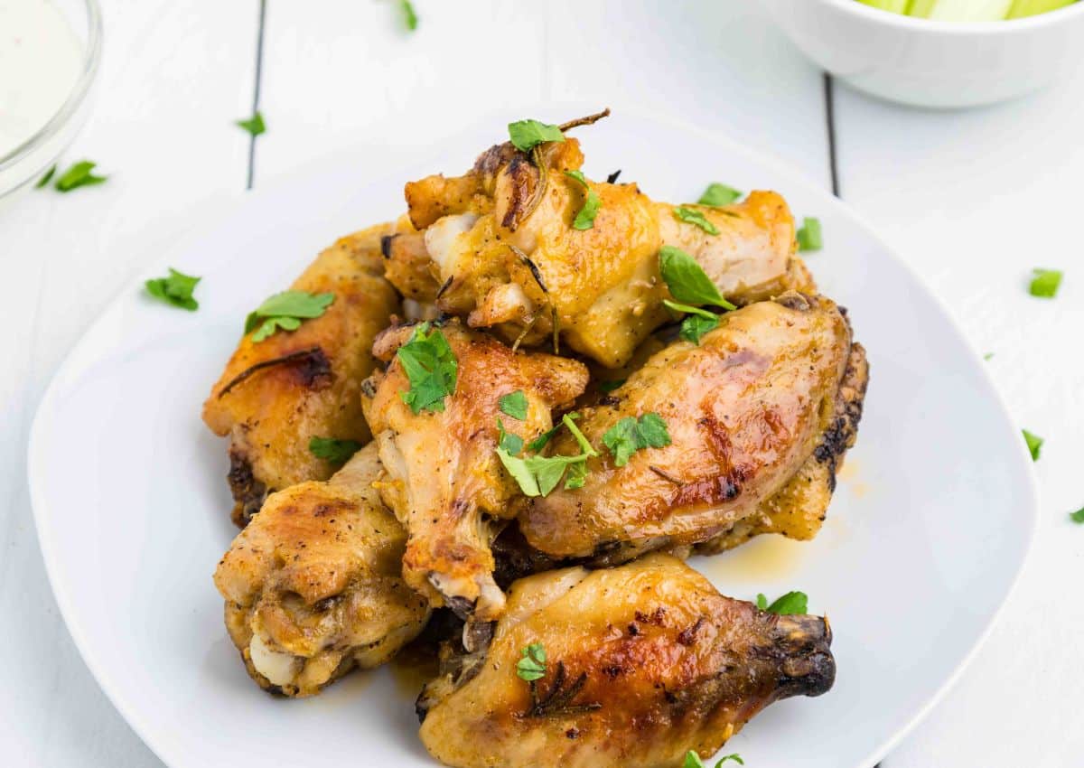 A white plate with several baked chicken wings garnished with chopped parsley, on a white table.